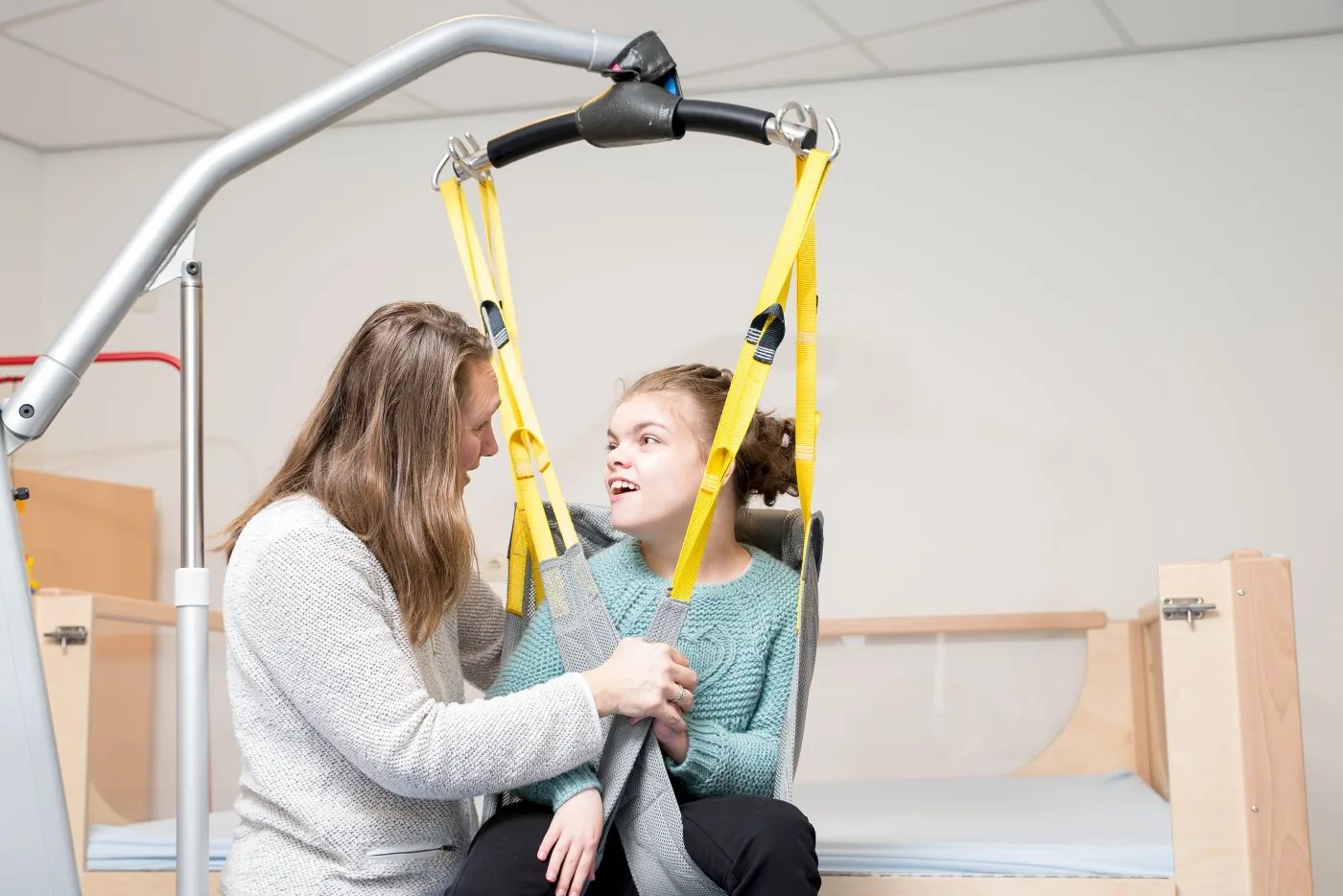A support worker assisting a young woman with a hoist transfer